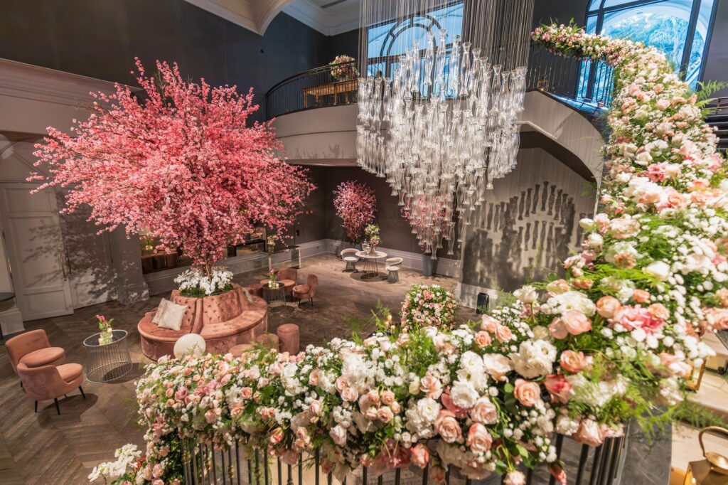 Luxurious wedding venue interior featuring blush-pink floral trees, cascading crystal chandelier and abundant rose arrangements creating an immersive rose-toned atmosphere