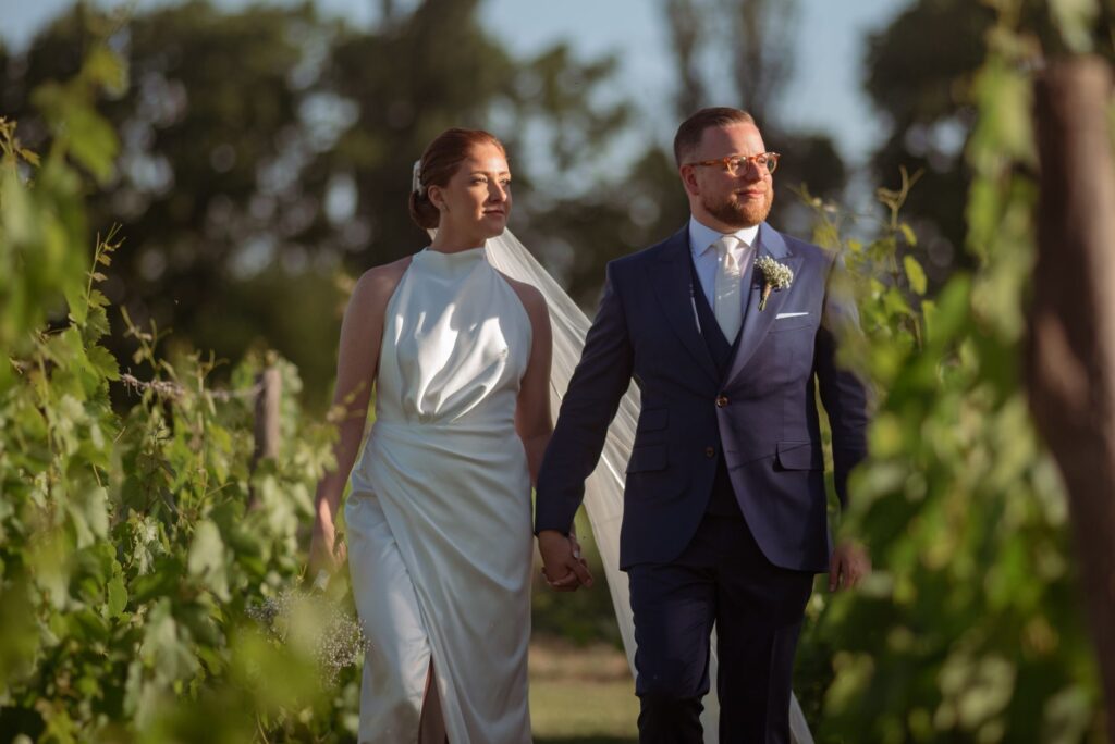 Bride and groom walking hand in hand through lush vineyard rows at a French estate wedding
