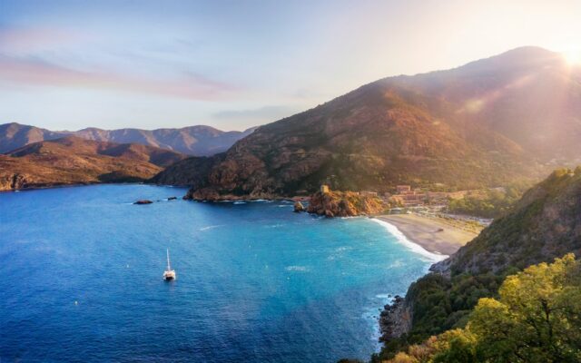 Sunlit Corsican bay with turquoise water, green mountains and a sailboat, ideal for a destination wedding in Corsica