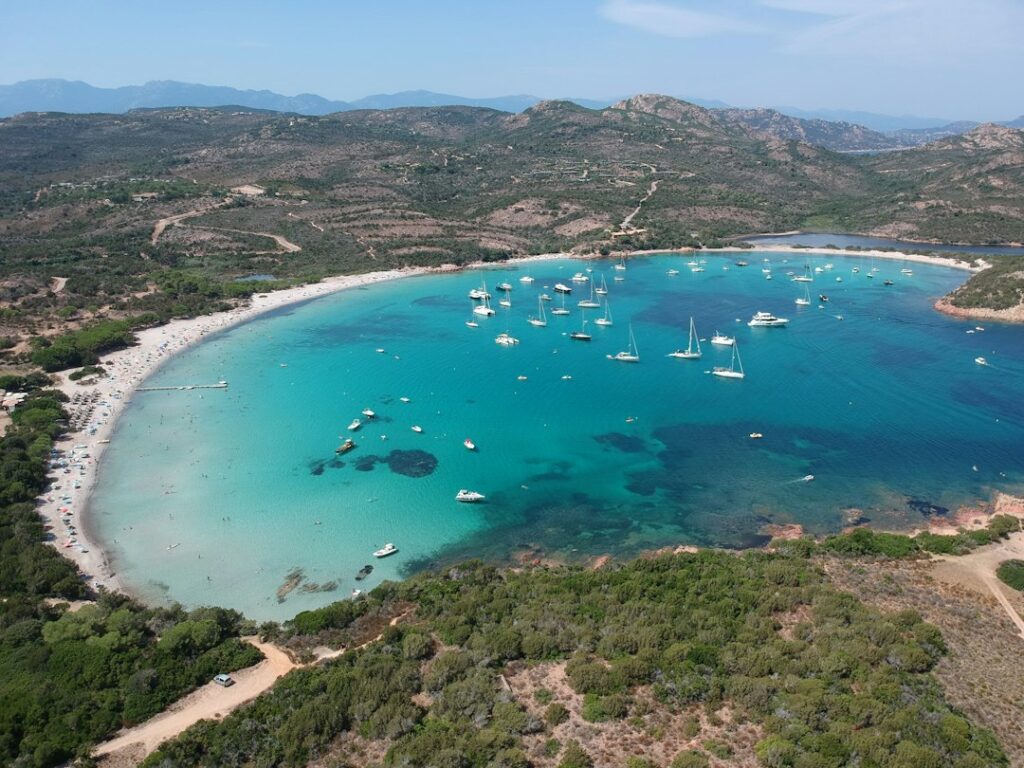 Aerial view of the Baie de la Rondinara near Bonifacio, Corsica, showing turquoise water, white sand beach and anchored sailboats