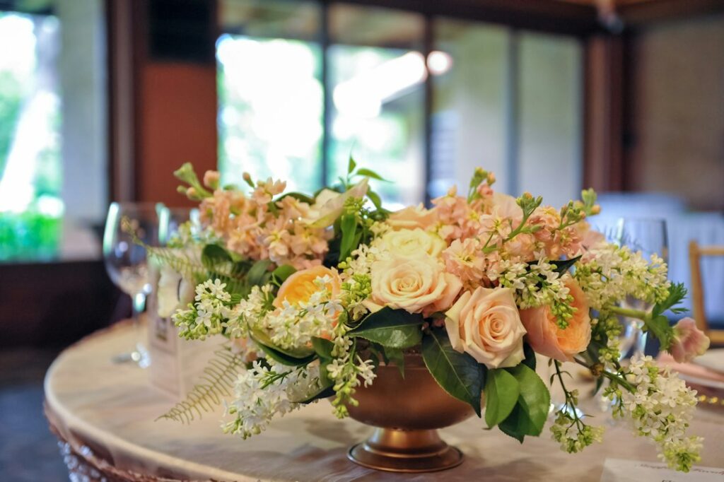 Elegant copper bowl centrepiece filled with blush and peach roses, soft white flowers and greenery on a wedding table