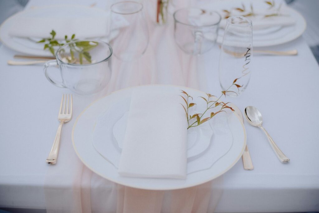 Elegant blush wedding tablescape with soft pink runner, white plates, crystal glassware and gold cutlery