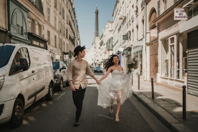 Bride and groom running joyfully through a Paris street with the Eiffel Tower in the background