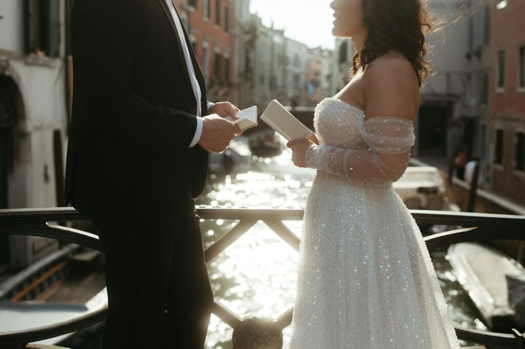 A couple exchanging wedding vows on a Venice canal bridge, the sun glittering on the water behind them