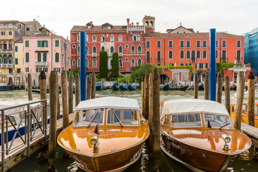 Two classic wooden water taxis moored at a private dock on the Grand Canal in Venice with a historic palazzo behind
